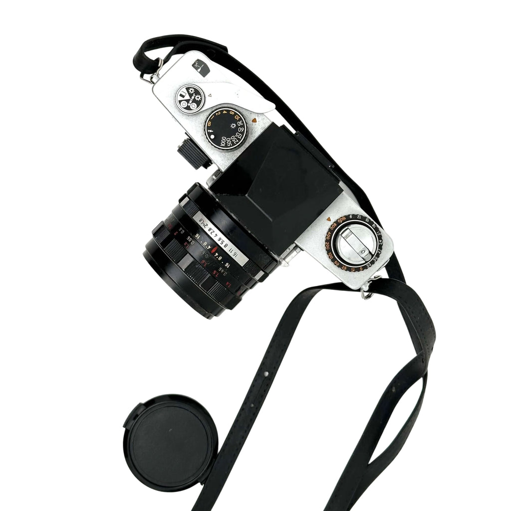 Silver-bodied film camera with a black lens and matching strap, featuring classic dials and controls.