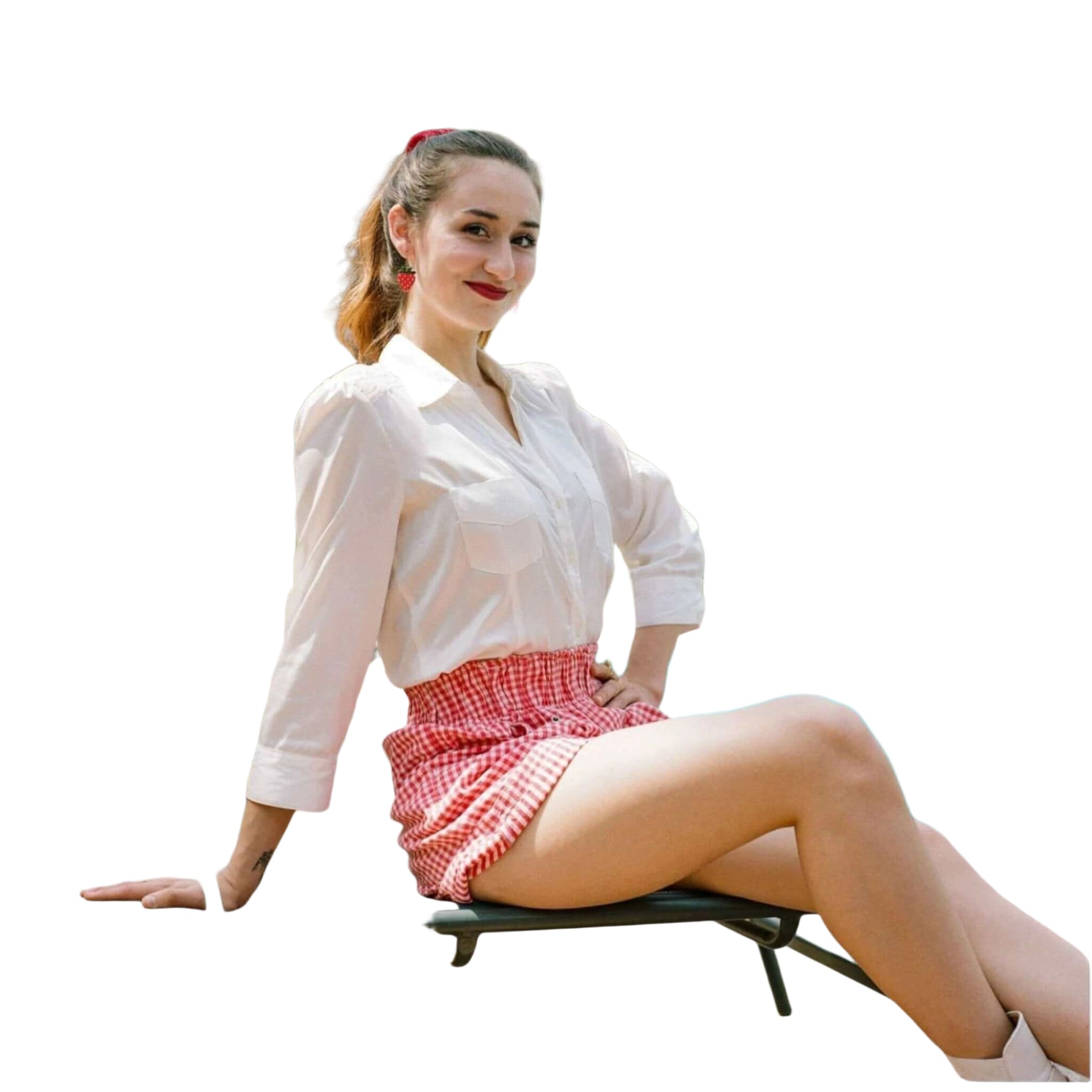 A woman wearing a white button-up shirt and red-and-white gingham shorts sits on a lounge chair by the pool.