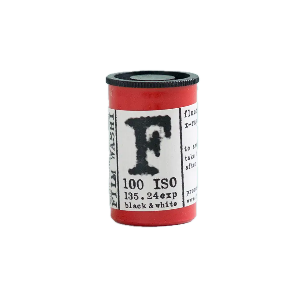 Red cylindrical film canister with a black ribbed cap and white label featuring bold black lettering, including ’film washi’ and ’100 iso,’ indicating it’s for black-and-white photography.