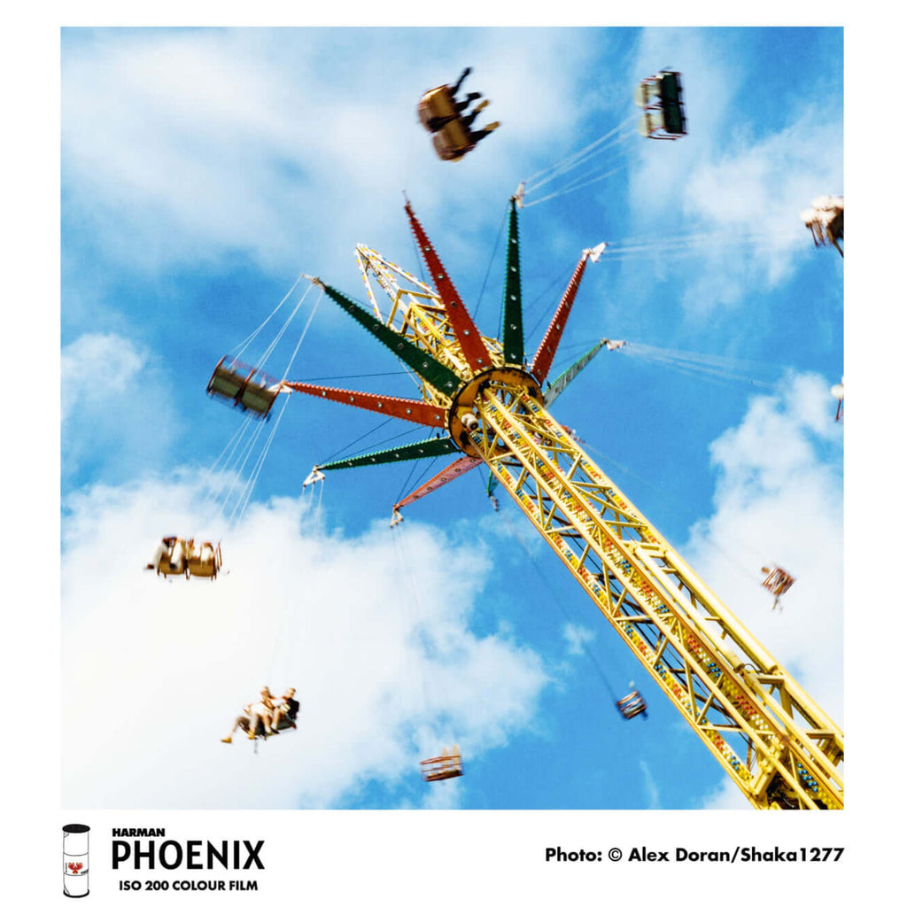 A vibrant yellow and green star-shaped amusement park ride with suspended seats against a bright blue sky.