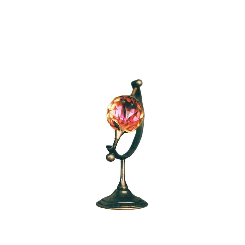 A miniature globe with a faceted, translucent pink crystal sphere mounted on an ornate metallic stand.