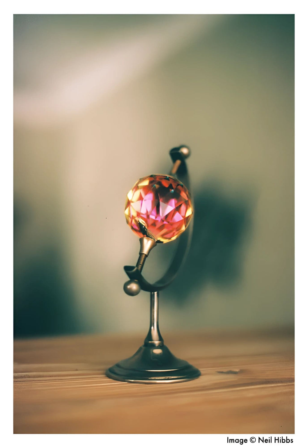 A miniature globe with a faceted, translucent pink crystal sphere mounted on an ornate metallic stand.
