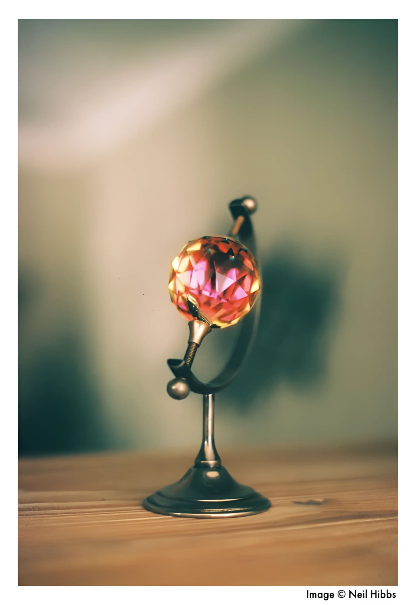 A miniature globe with a faceted, translucent pink crystal sphere mounted on an ornate metallic stand.
