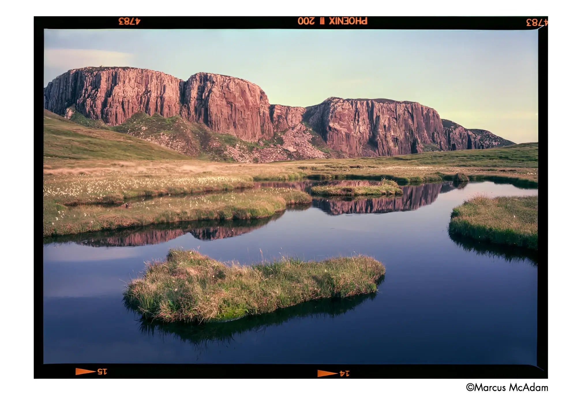 The image features a majestic, rugged cliff face with reddish-brown rock formations rising prominently against the sky.