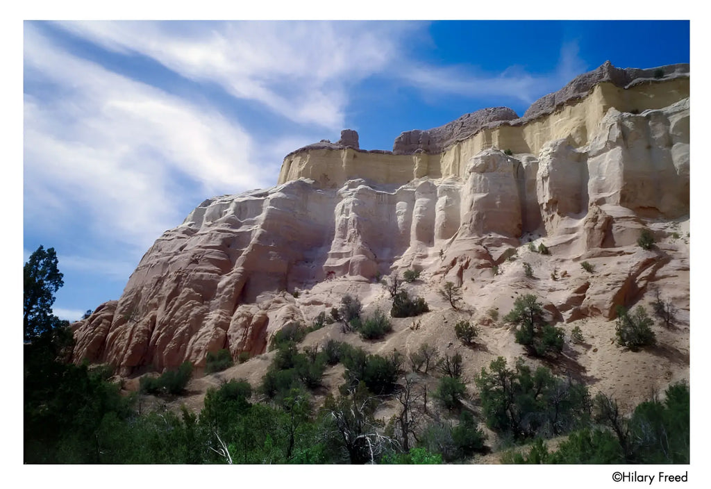 Towering sandstone cliffs with layered hues of beige, tan, and pale yellow under a bright blue sky.