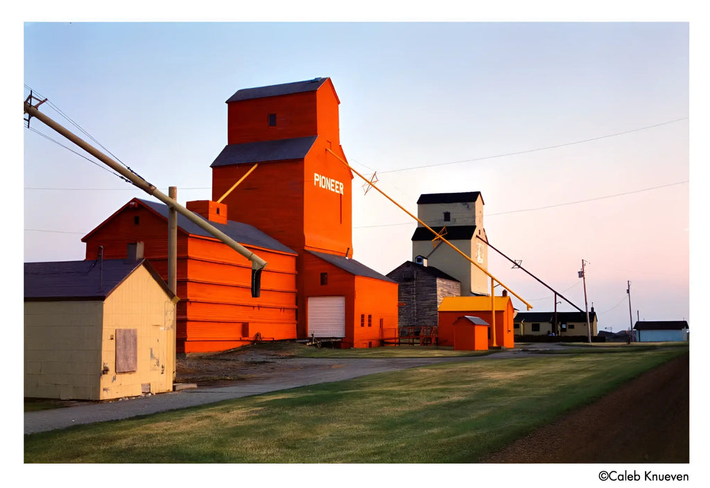 A tall, vibrant orange grain elevator with a dark gray roof and the word ’pioneer’ painted in white on its side.