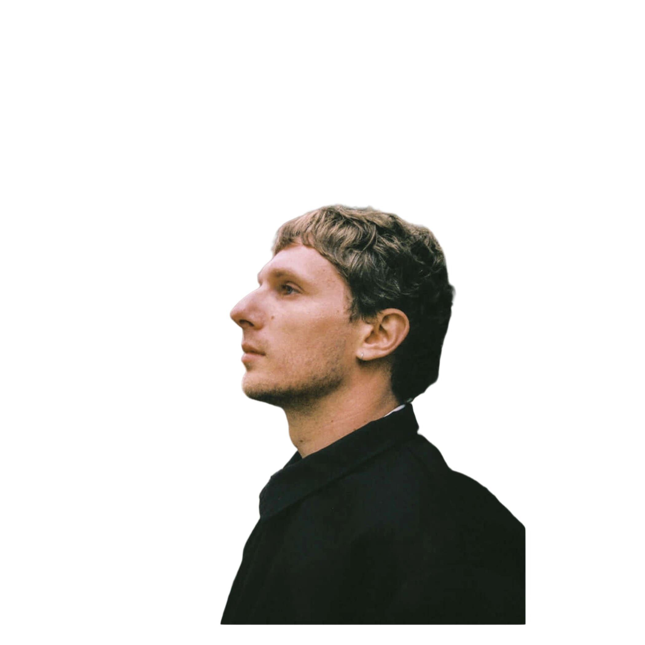 A man with short brown hair and a light stubble, wearing a black coat.