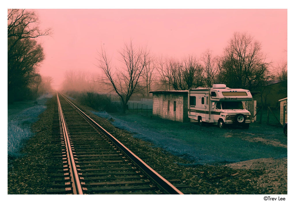 White and beige rv parked beside a small shed under a pink-hued sky.