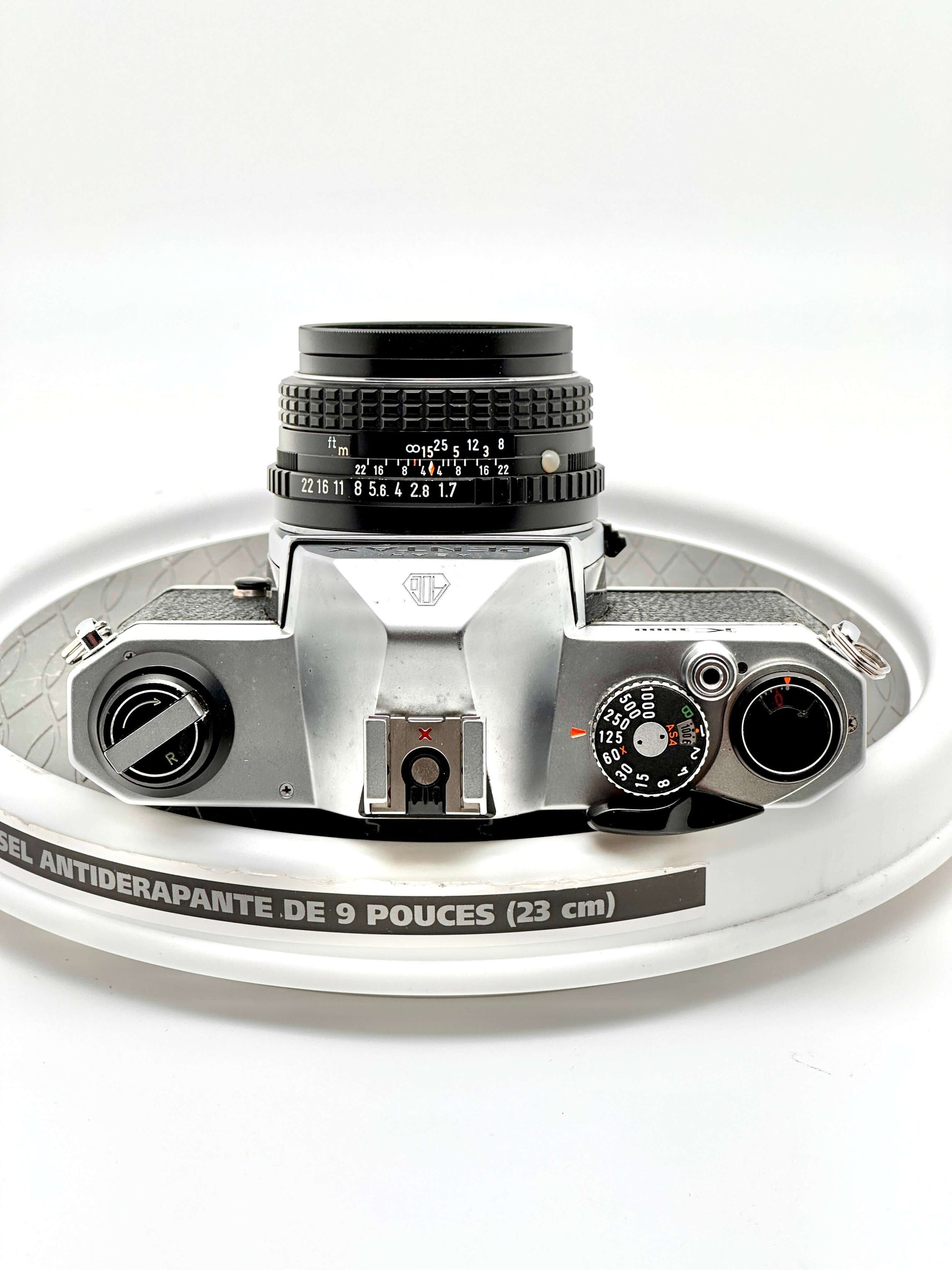 Top view of Japanese Pentax K1000 35mm film camera with 50mm f1.7 lens on a circular surface.