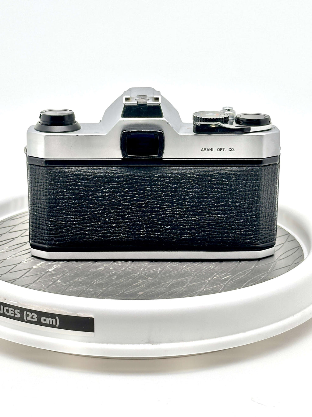 Pentax K1000 black 35mm film camera back view on a round display, showcasing robust design and vintage aesthetic.