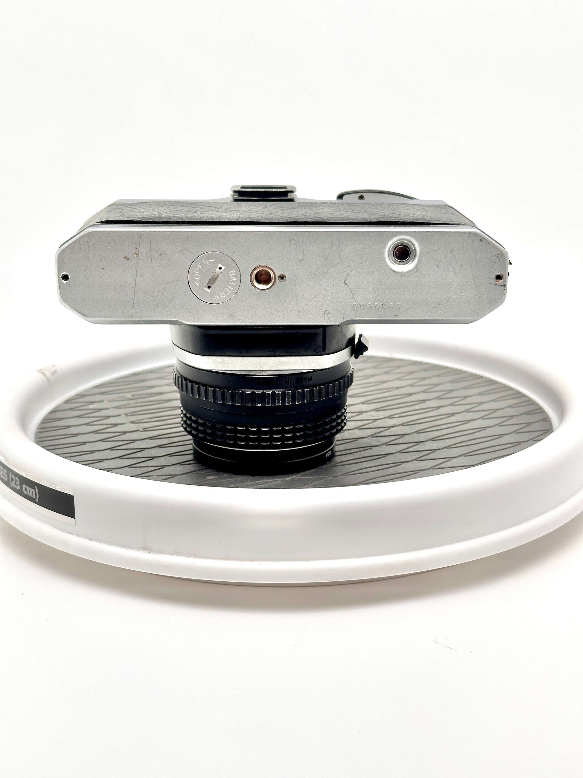 Top view of Japanese Asahi Pentax K1000 black 35mm film camera with 50mm f2 lens on white display stand.