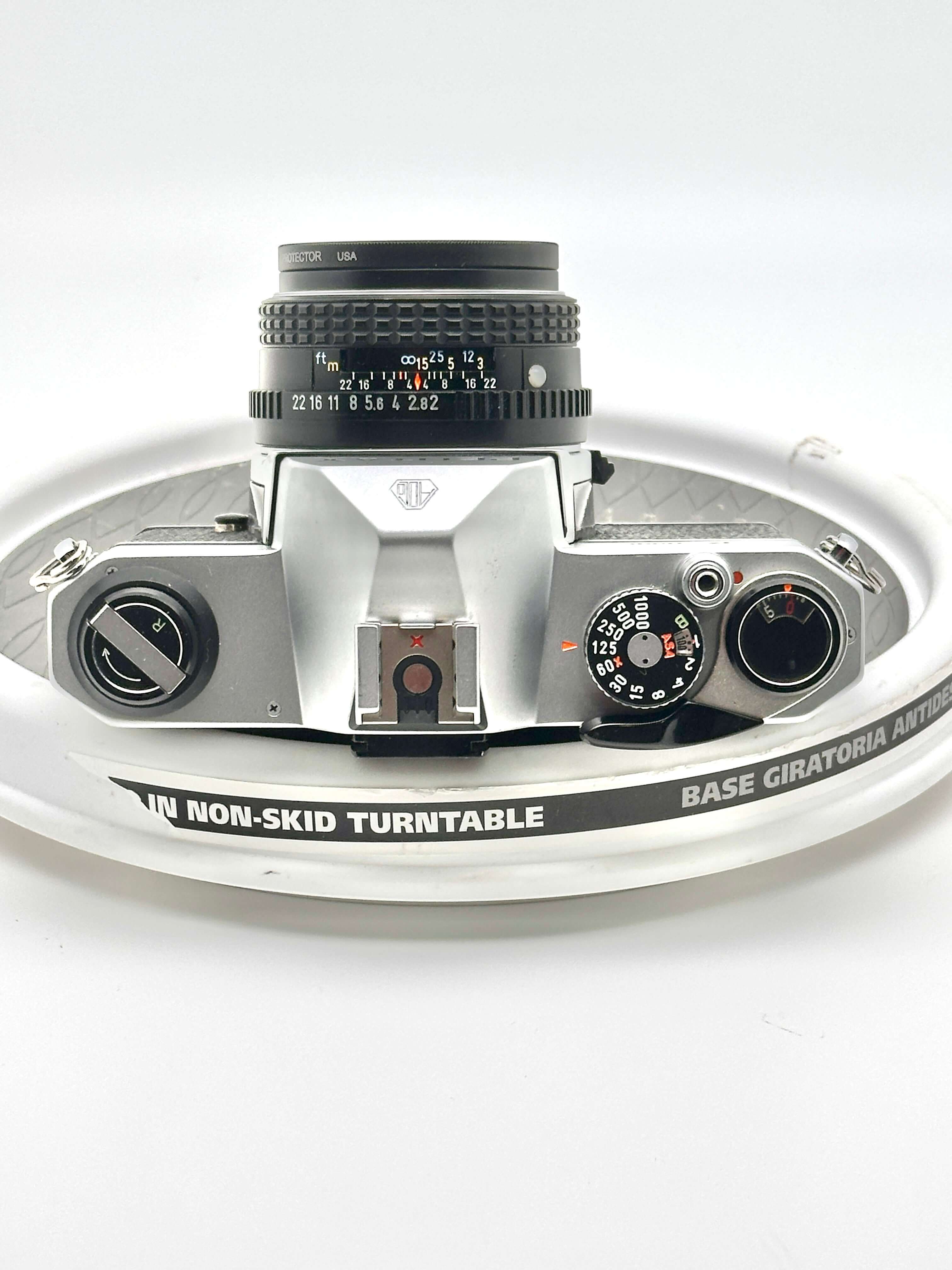 Top view of a Pentax K1000 black 35mm film camera with 50mm f2 lens on a non-skid turntable.