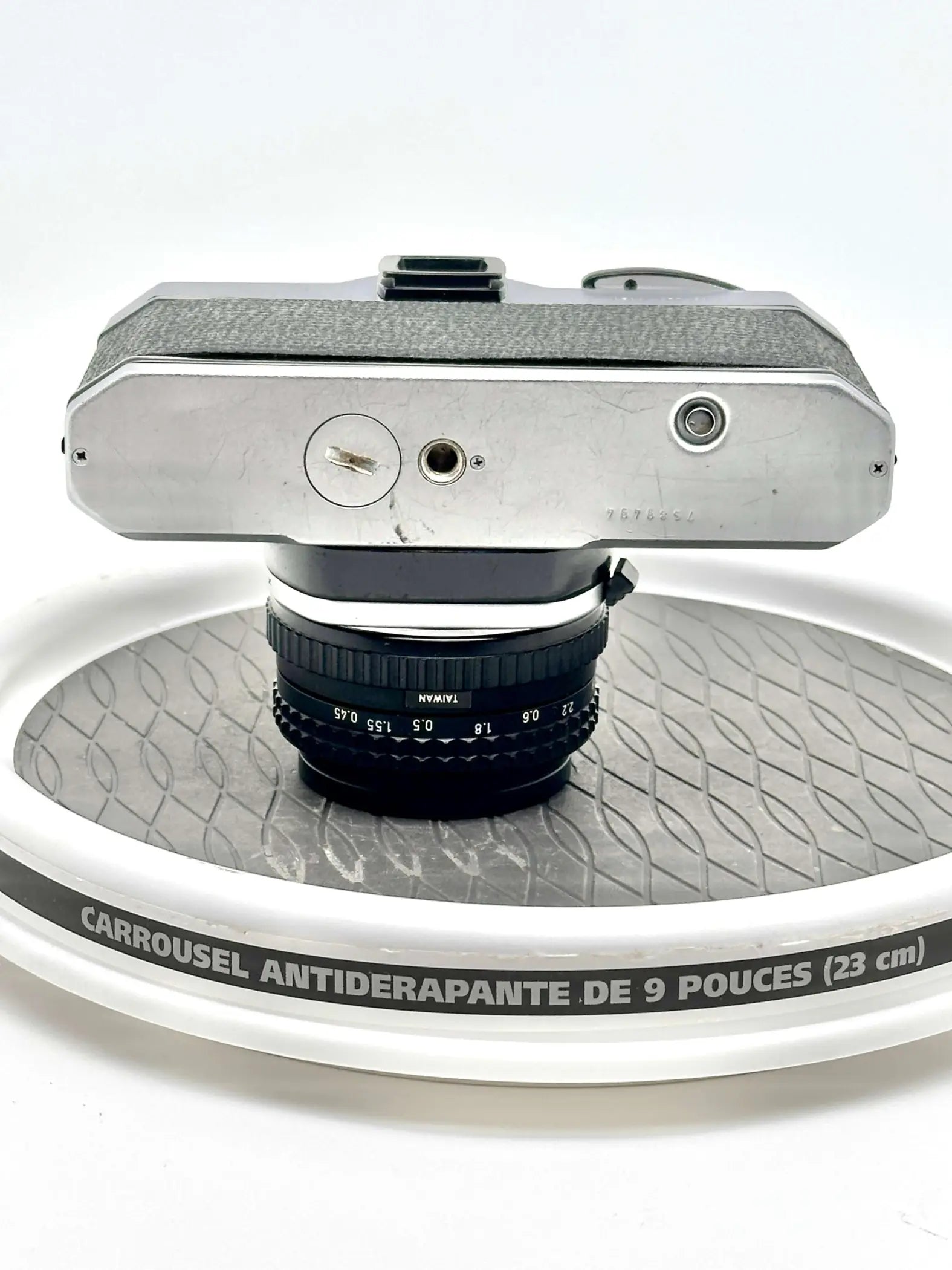 Silver-bodied vintage camera with a black lens marked ’taiwan’ resting on a white rotating display stand.