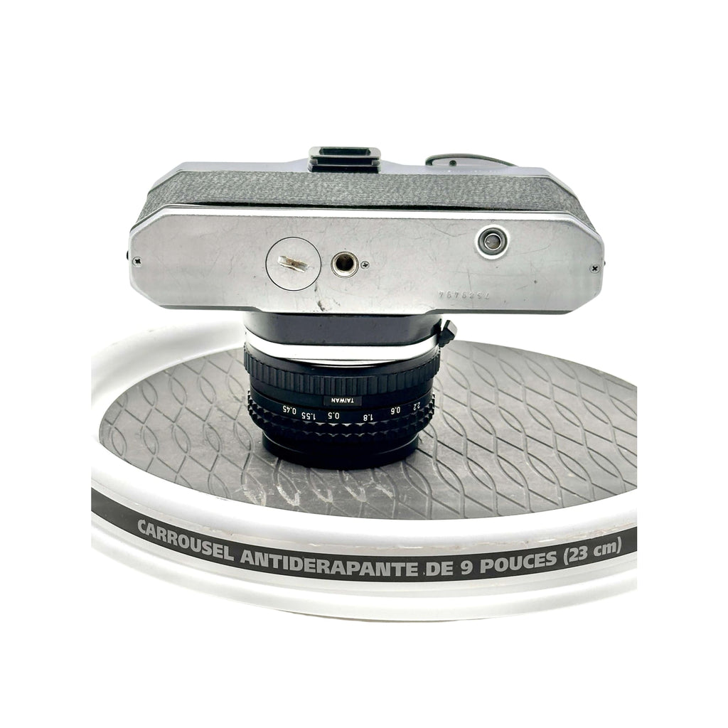 Silver-bodied vintage camera with a black lens marked ’taiwan’ resting on a white rotating display stand.