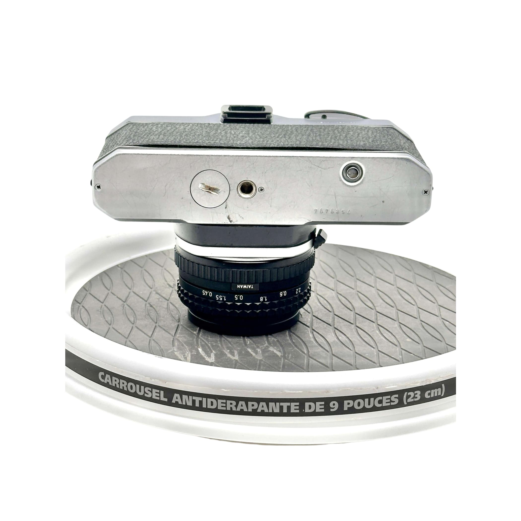 Silver-bodied vintage camera with a black lens marked ’taiwan’ resting on a white rotating display stand.