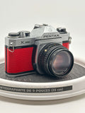 Asahi Pentax K1000 red used 35mm film camera with 50mm f1.7 lens on display.