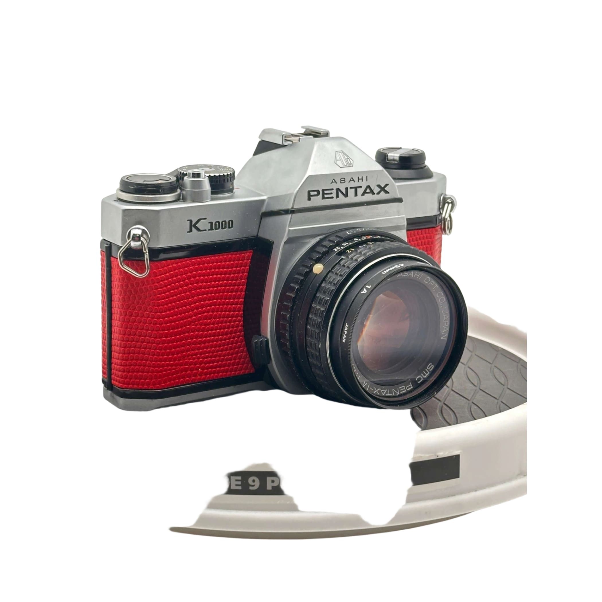 Silver and red asahi pentax k1000 film camera with textured leather grip.