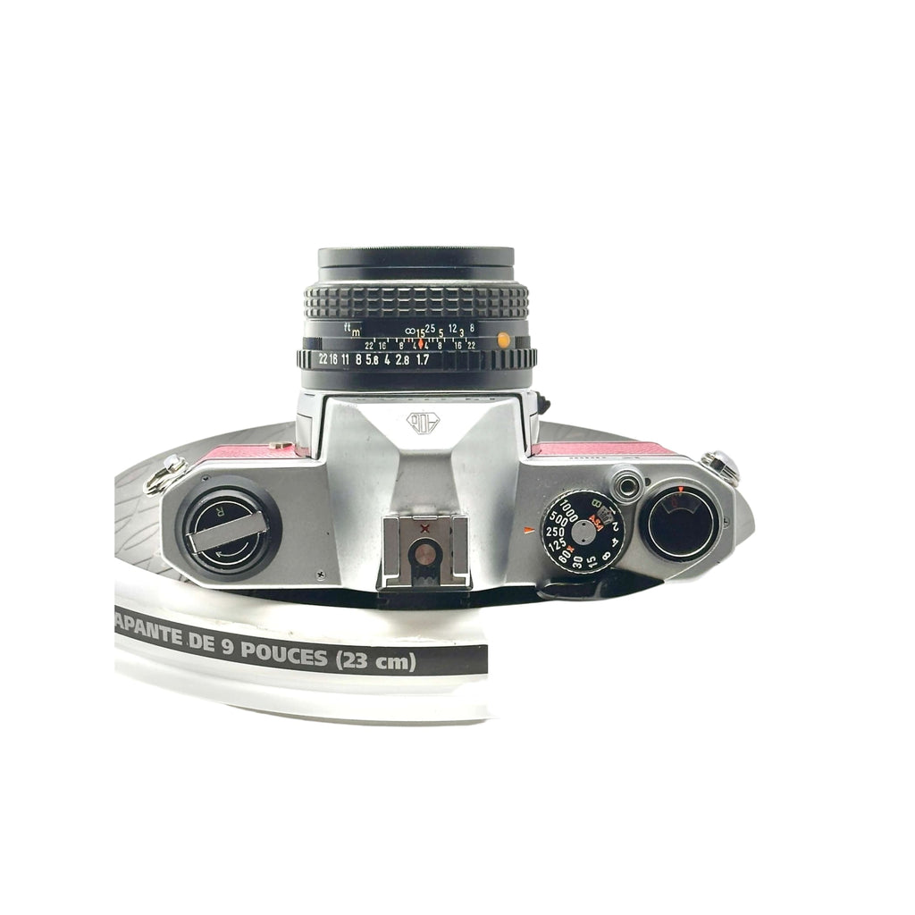 Silver-bodied rangefinder camera with a black lens and pink accents on the top plate.