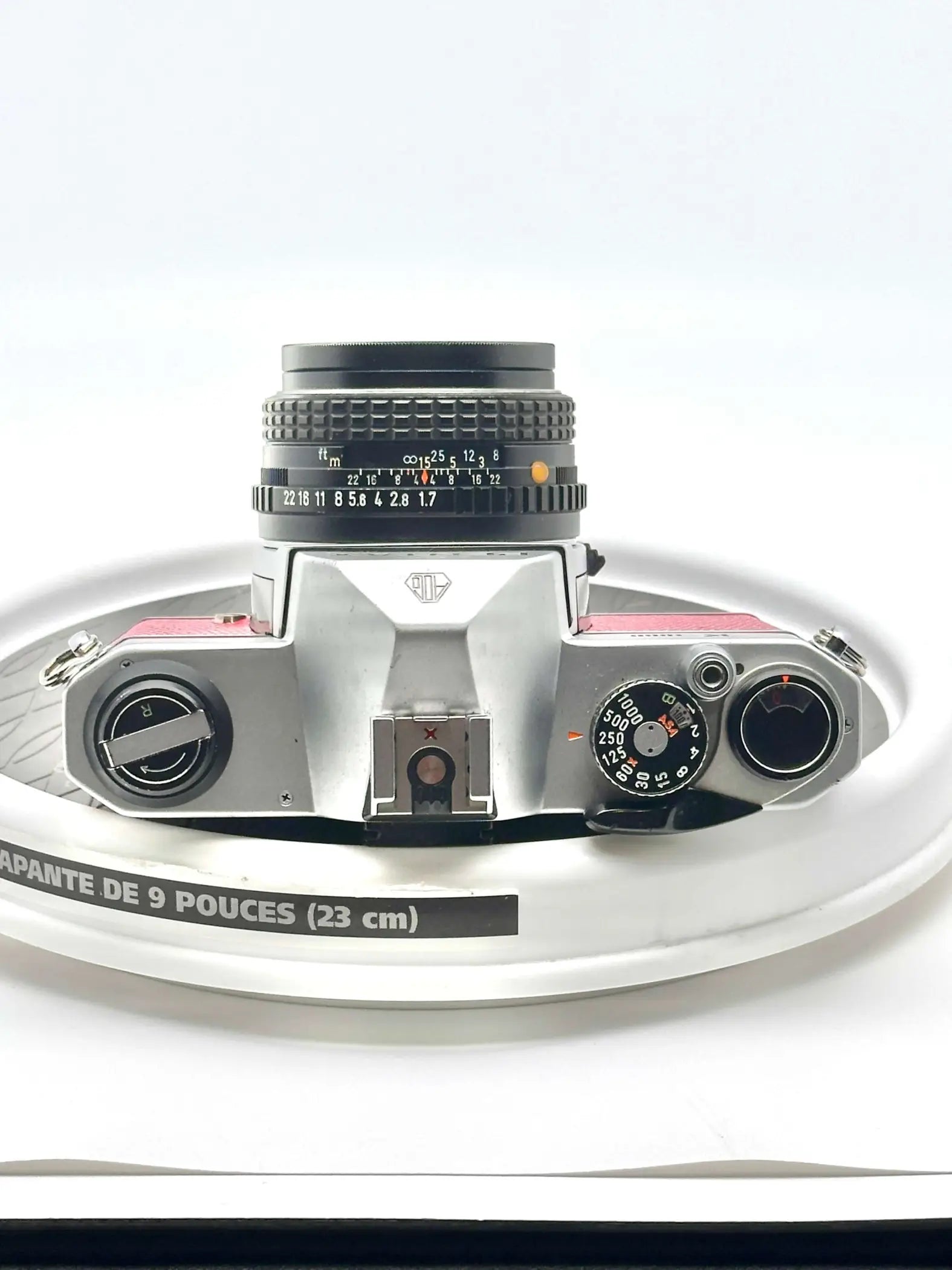 Silver-bodied rangefinder camera with a black lens and pink accents on the top plate.