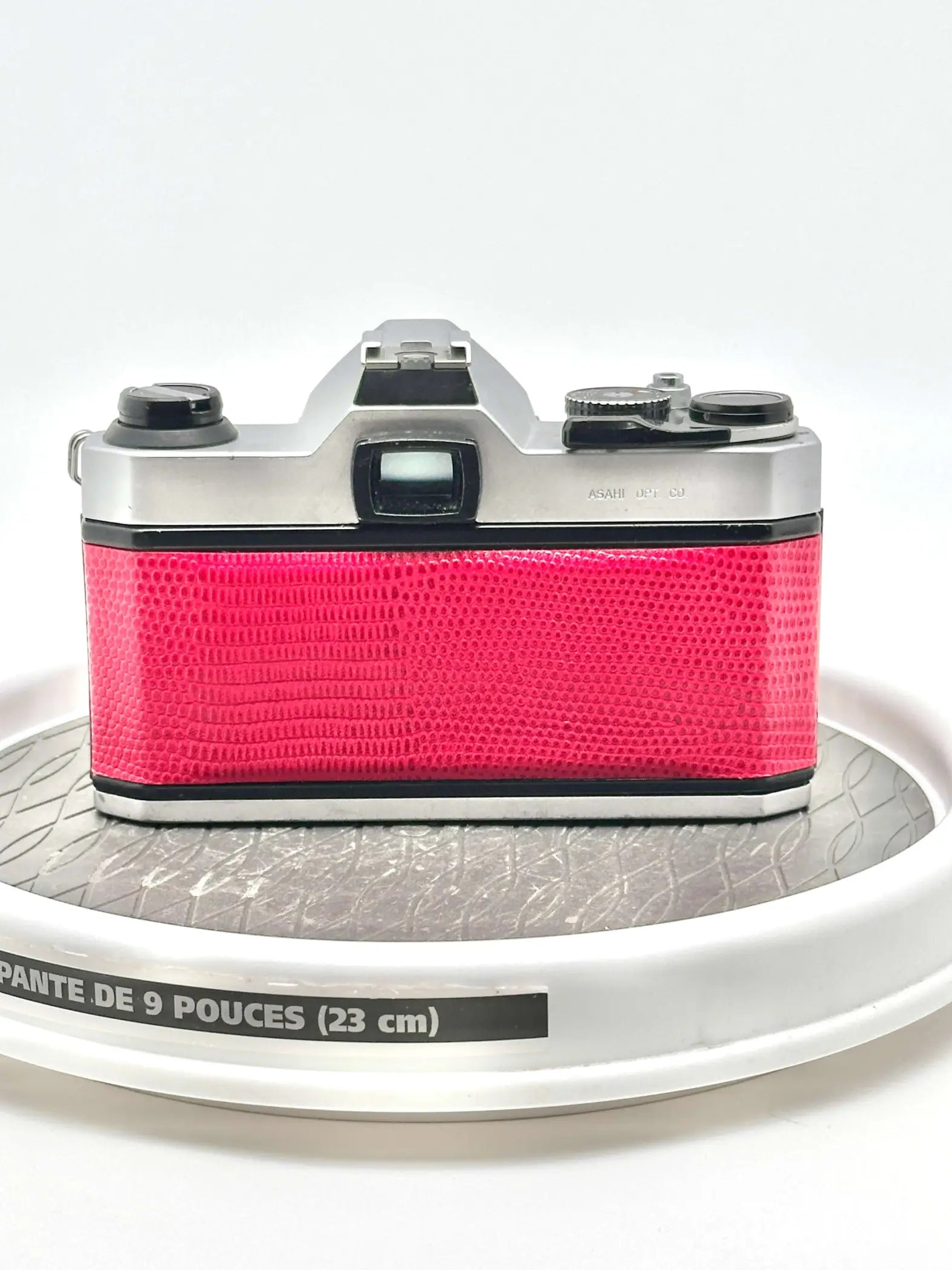 A vibrant pink camera with a textured, reptile-skin patterned body and silver metallic top plate.