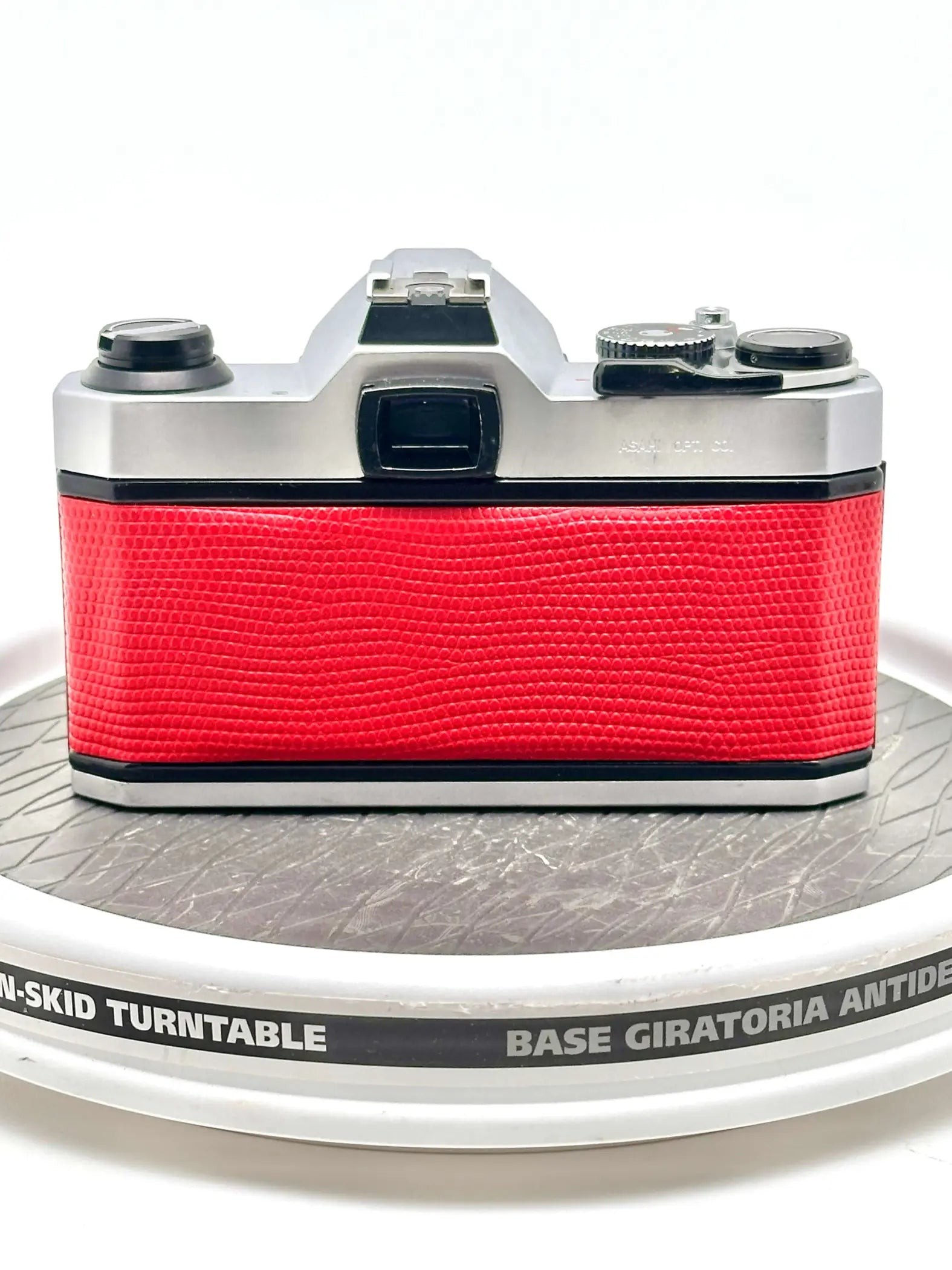 A vintage silver-bodied camera with a vibrant red textured leather grip.
