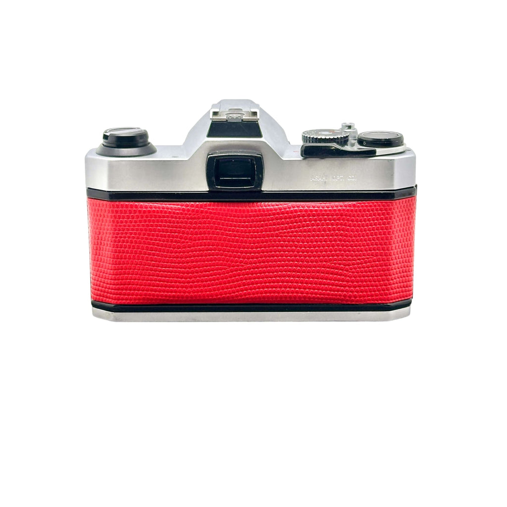 A vintage silver-bodied camera with a vibrant red textured leather grip.
