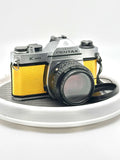 Silver and yellow asahi pentax k1000 film camera with a textured leather grip.