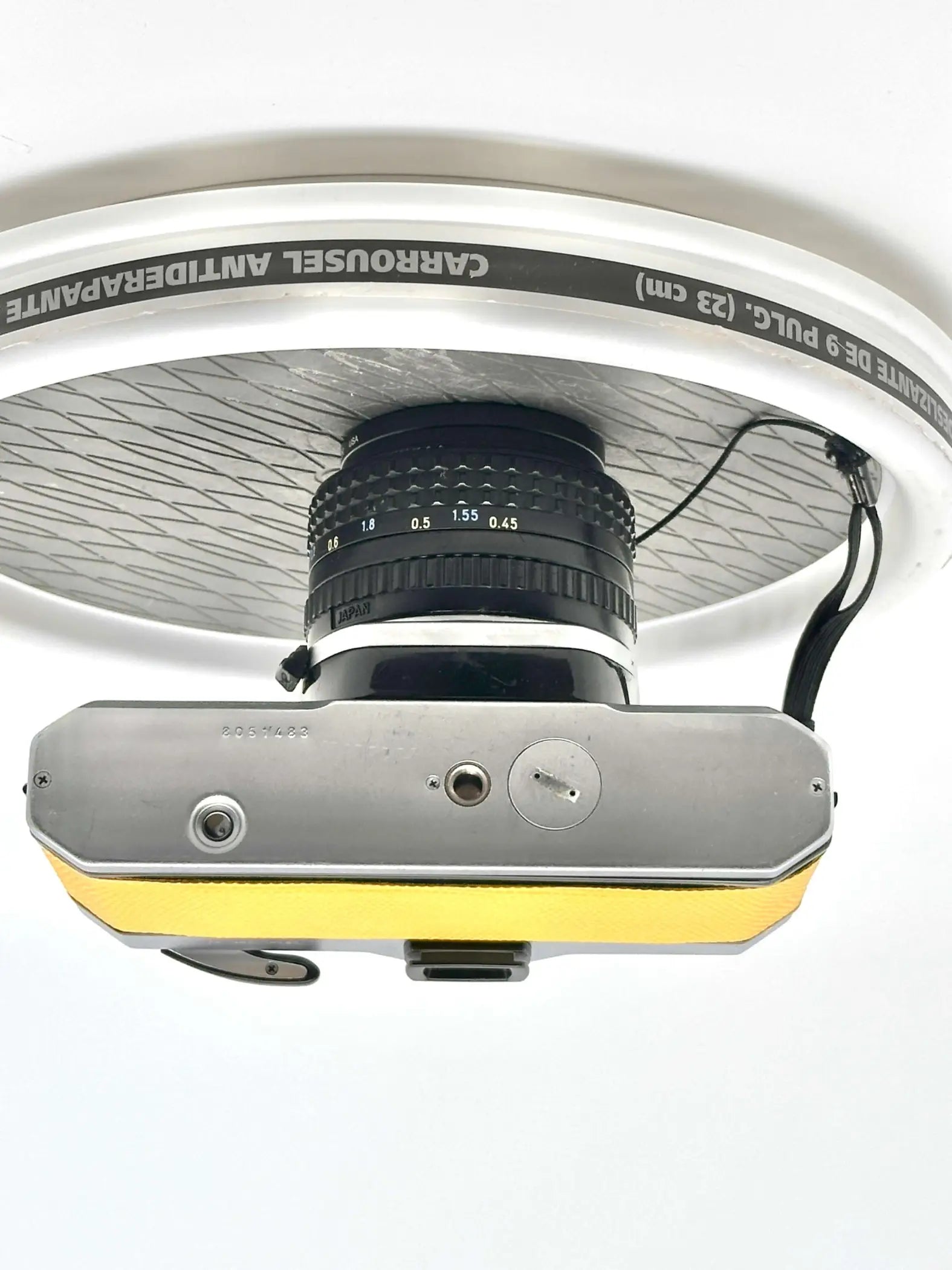 Silver and yellow vintage camera with a black lens mounted beneath a white bicycle wheel rim.