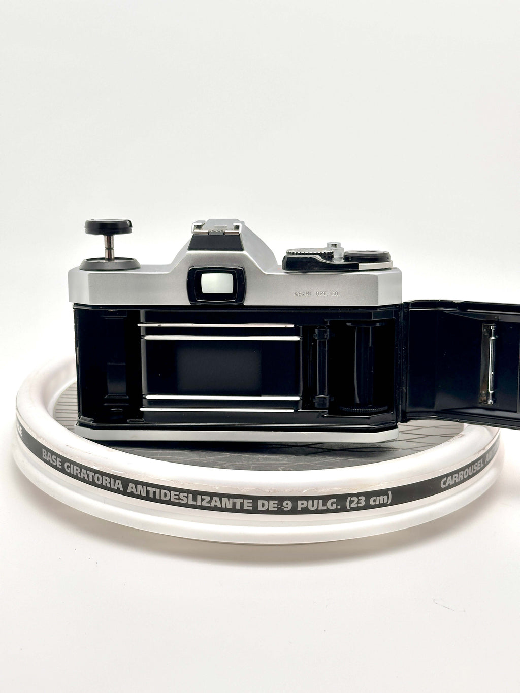 Pentax K1000 35mm film camera with opened back and film compartment on a circular surface.