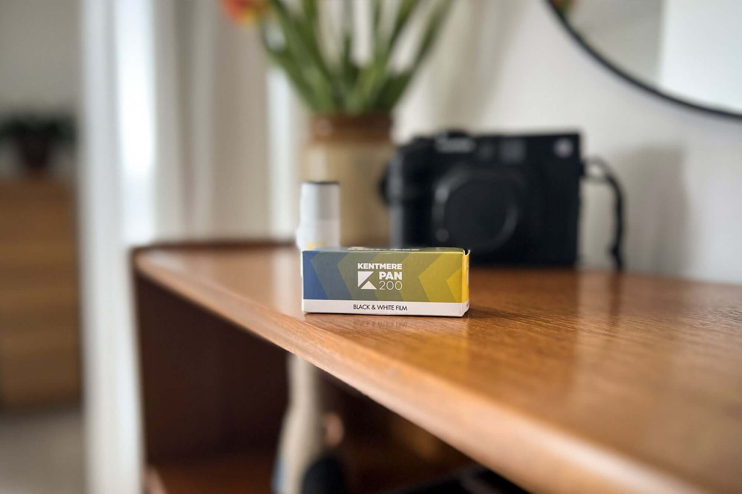 Kentmere Pan 200 black and white 120 film box on a wooden shelf with a camera in background.