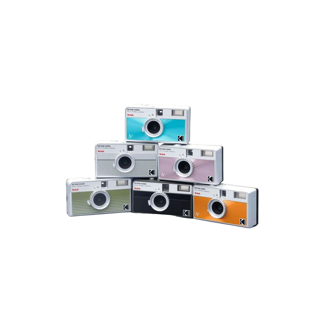 A stack of six kodak instamatic n instant cameras in assorted vibrant colors including teal, silver, pink, green, black, and orange.
