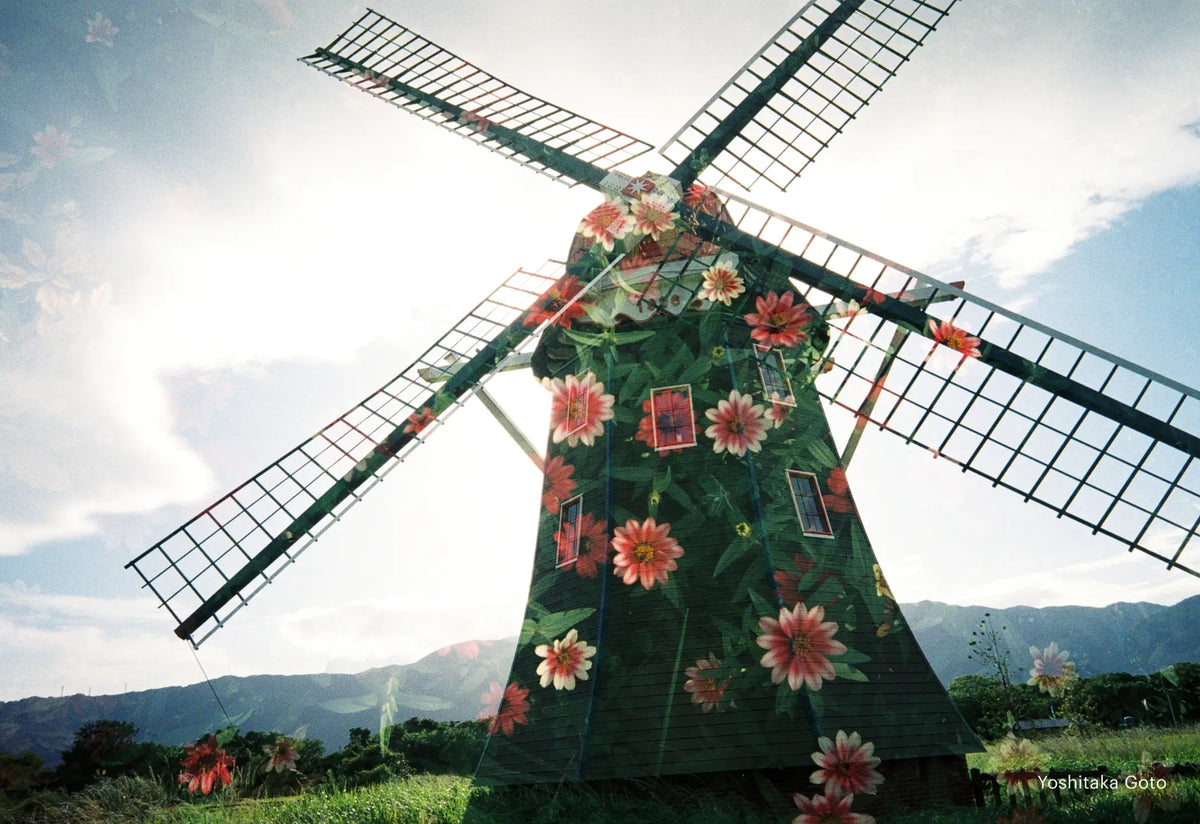 A green windmill adorned with vibrant pink and orange flowers, featuring a painted design on its wooden structure.
