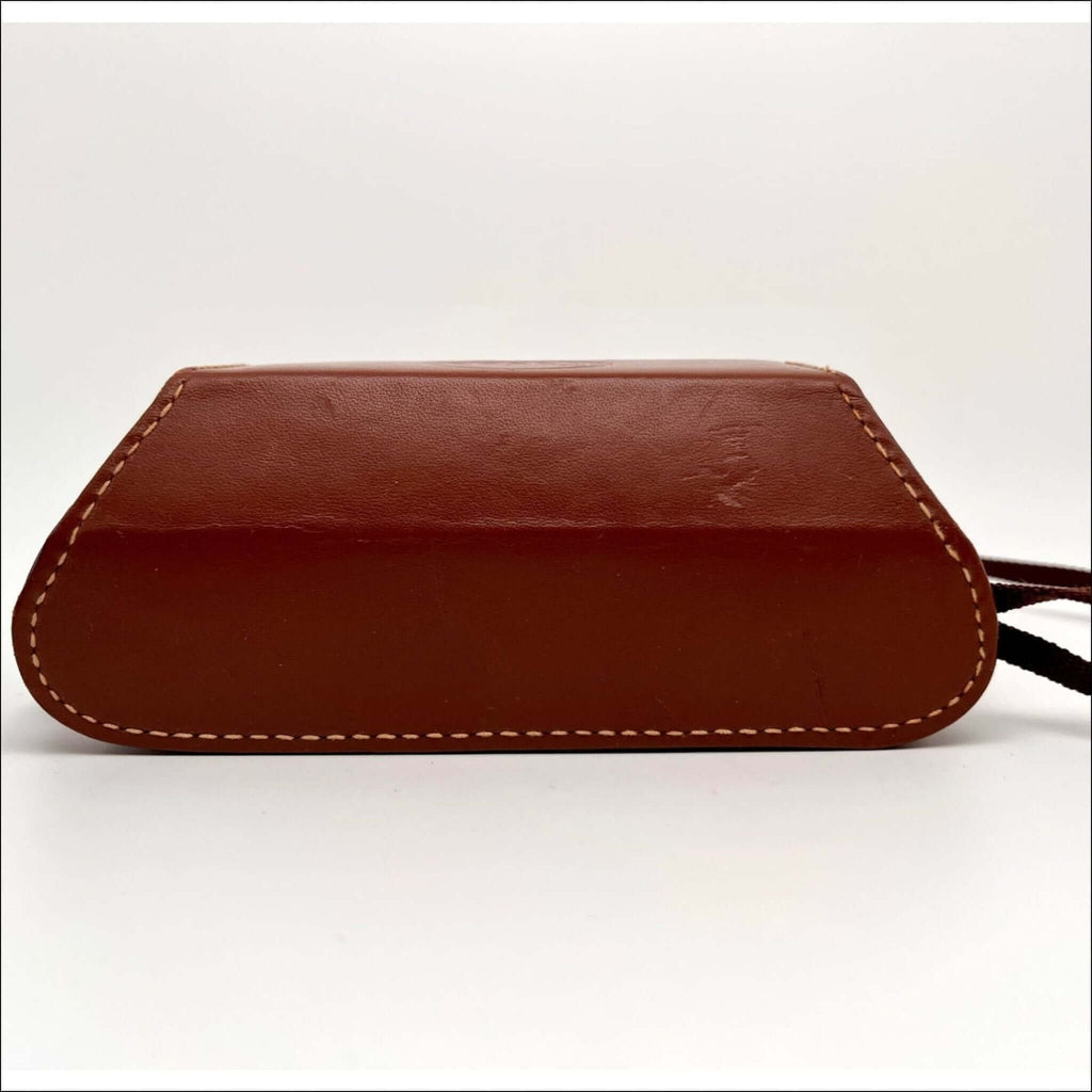 Brown leather camera case with contrasting white stitching and a black strap.