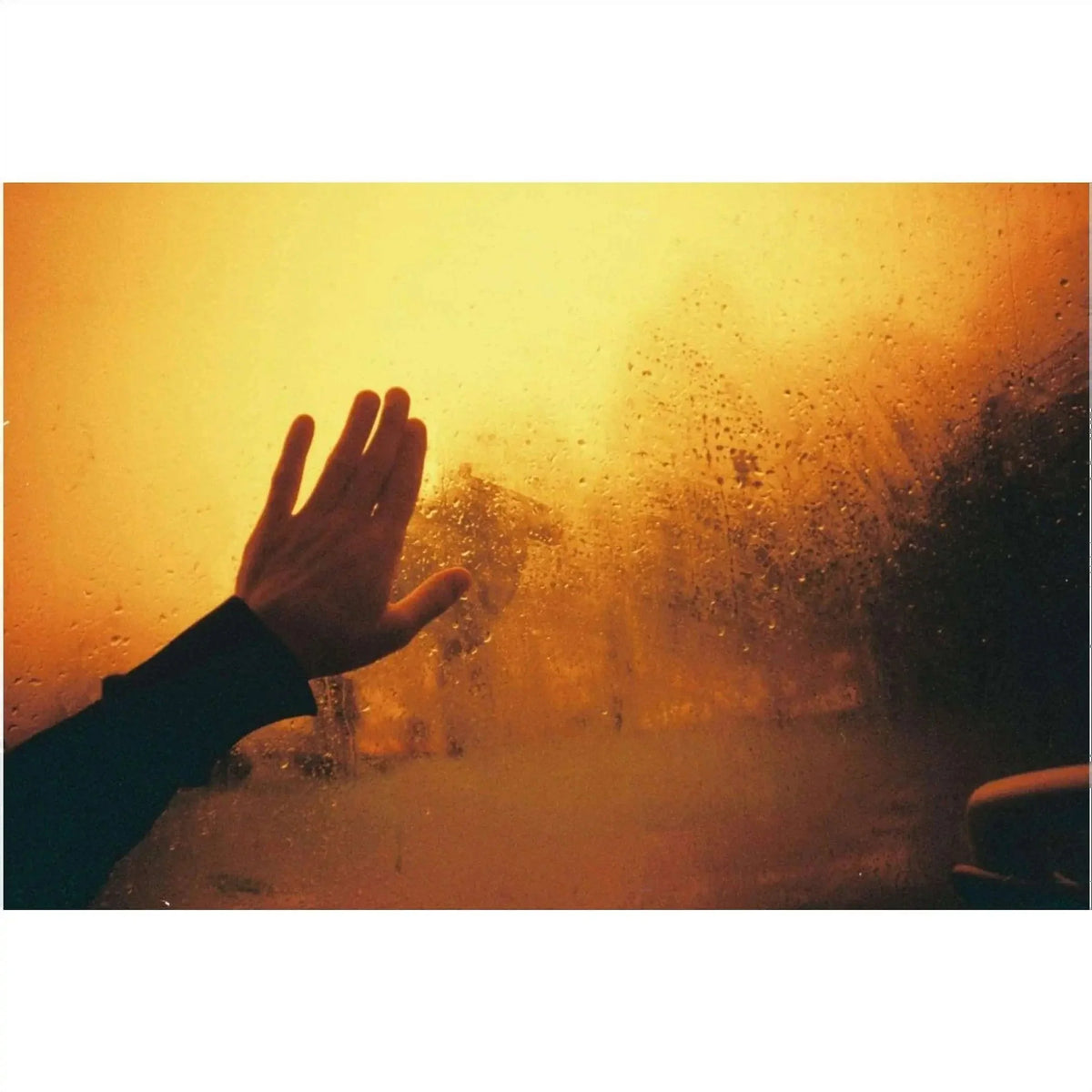 A hand pressed against a fogged-up window, fingers spread as if reaching out through the warm, golden haze.