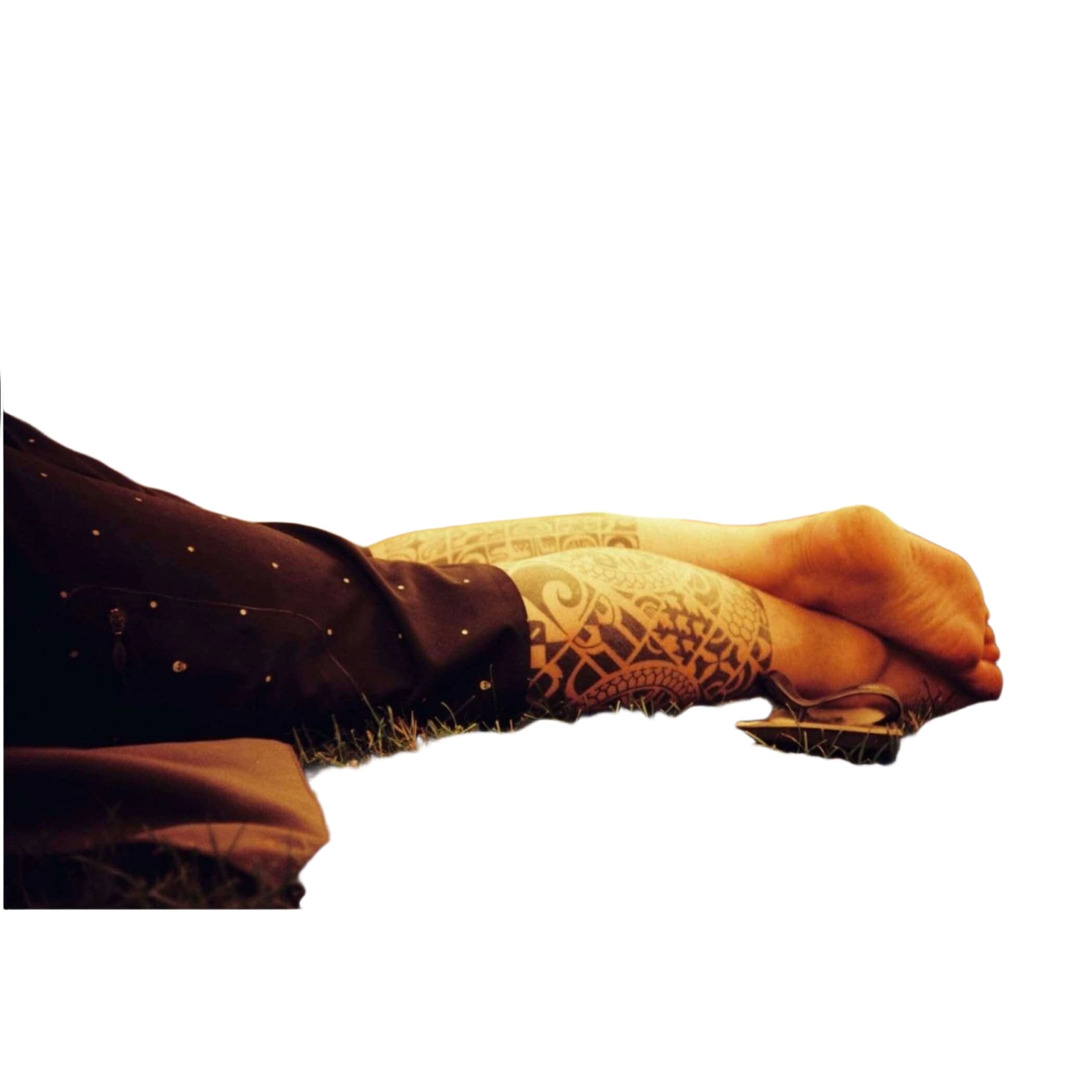 A person’s tattooed forearm and hand resting on grass, featuring intricate black tribal-style patterns.