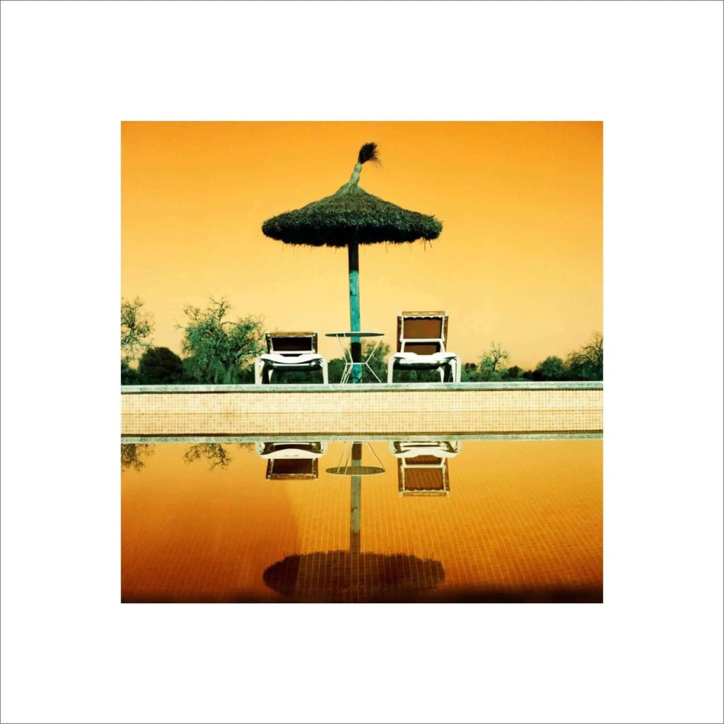 A thatched umbrella with a green pole stands beside two white lounge chairs by the poolside.