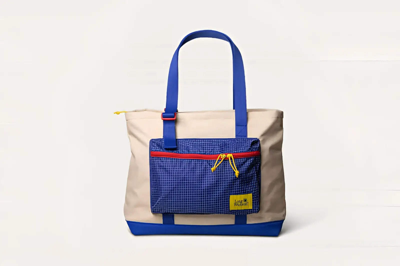 Beige and blue canvas tote bag with a grid-patterned front pocket, red zipper trim, yellow drawstrings, and matching blue handles.
