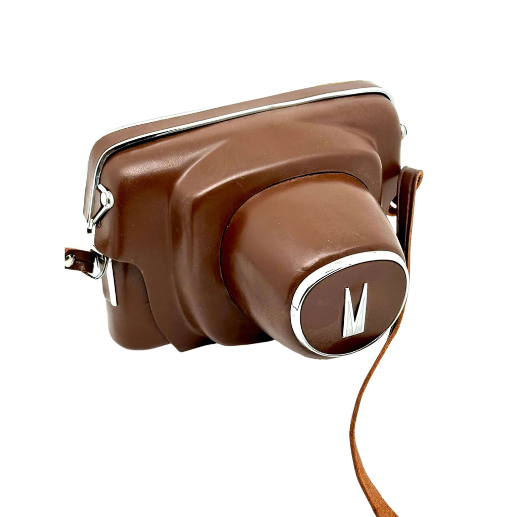 Brown leather camera case with a silver ’m’ logo on the lens cover and matching strap.