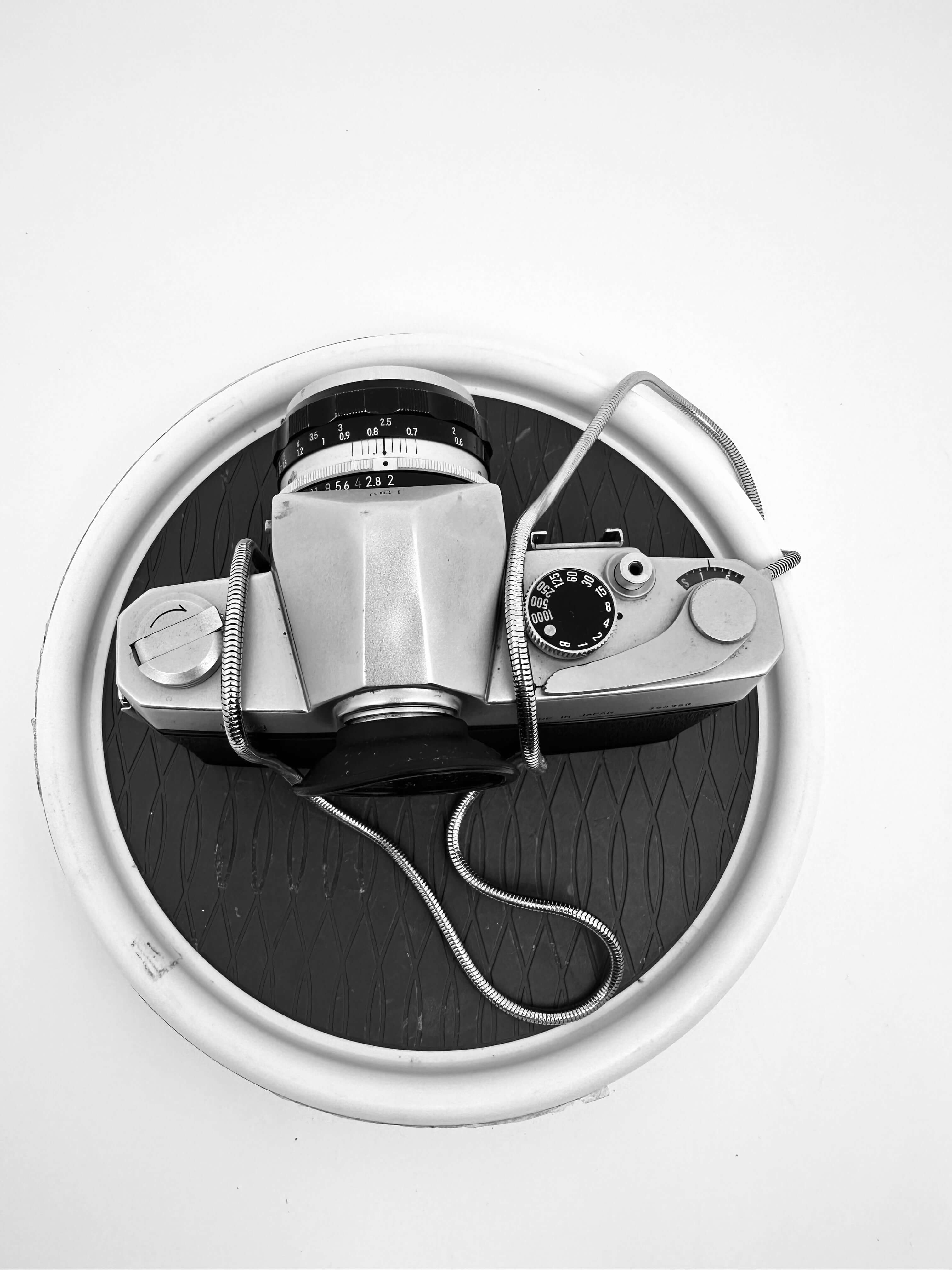 Nikkorex F 35mm film camera with 35mm f/2.8 lens on a black circular surface.