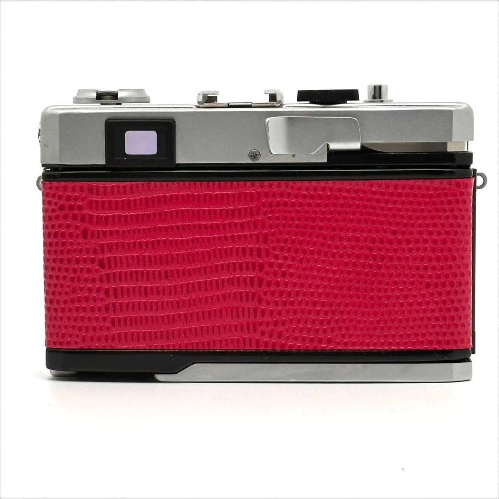 Red crocodile-textured body with silver top and black accents, classic film camera design.