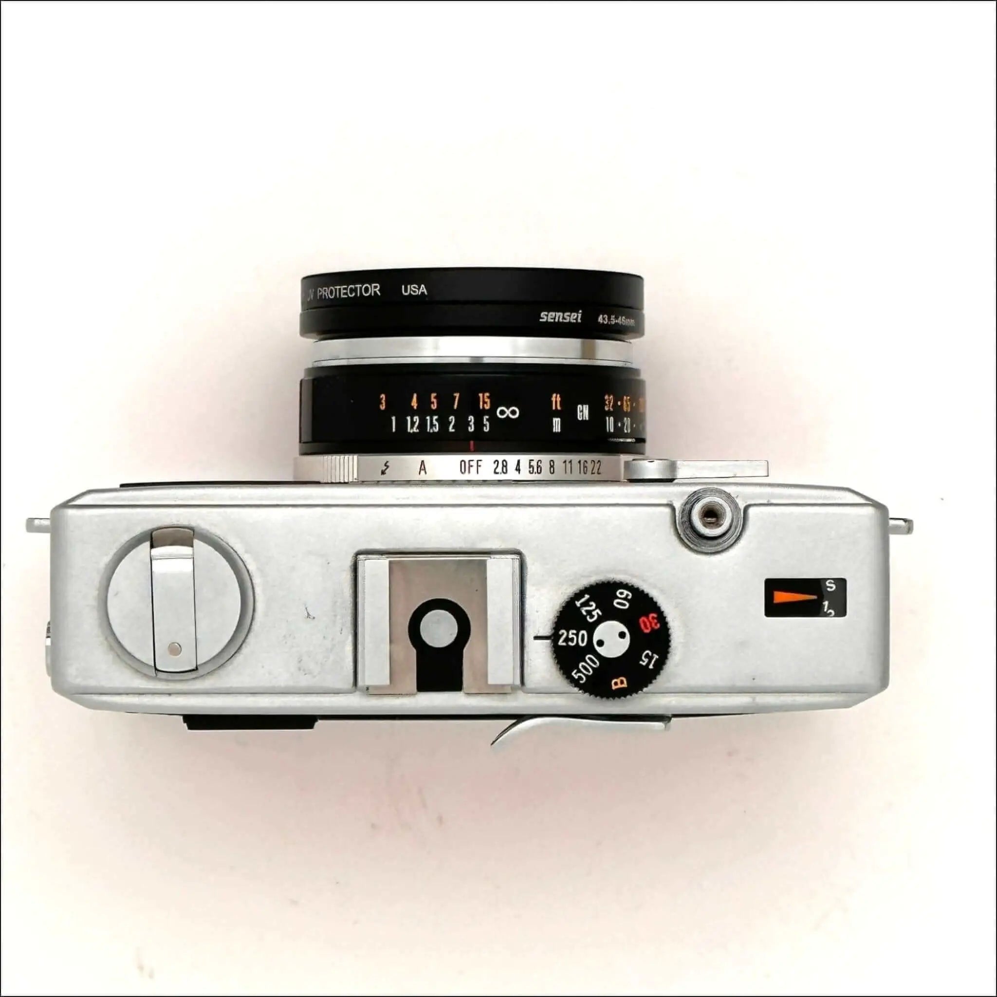 Silver-bodied rangefinder camera with a black and silver lens marked ’sensei 43-5.6mm’ mounted on top, featuring manual focus dials and shutter speed settings visible on its side panel.