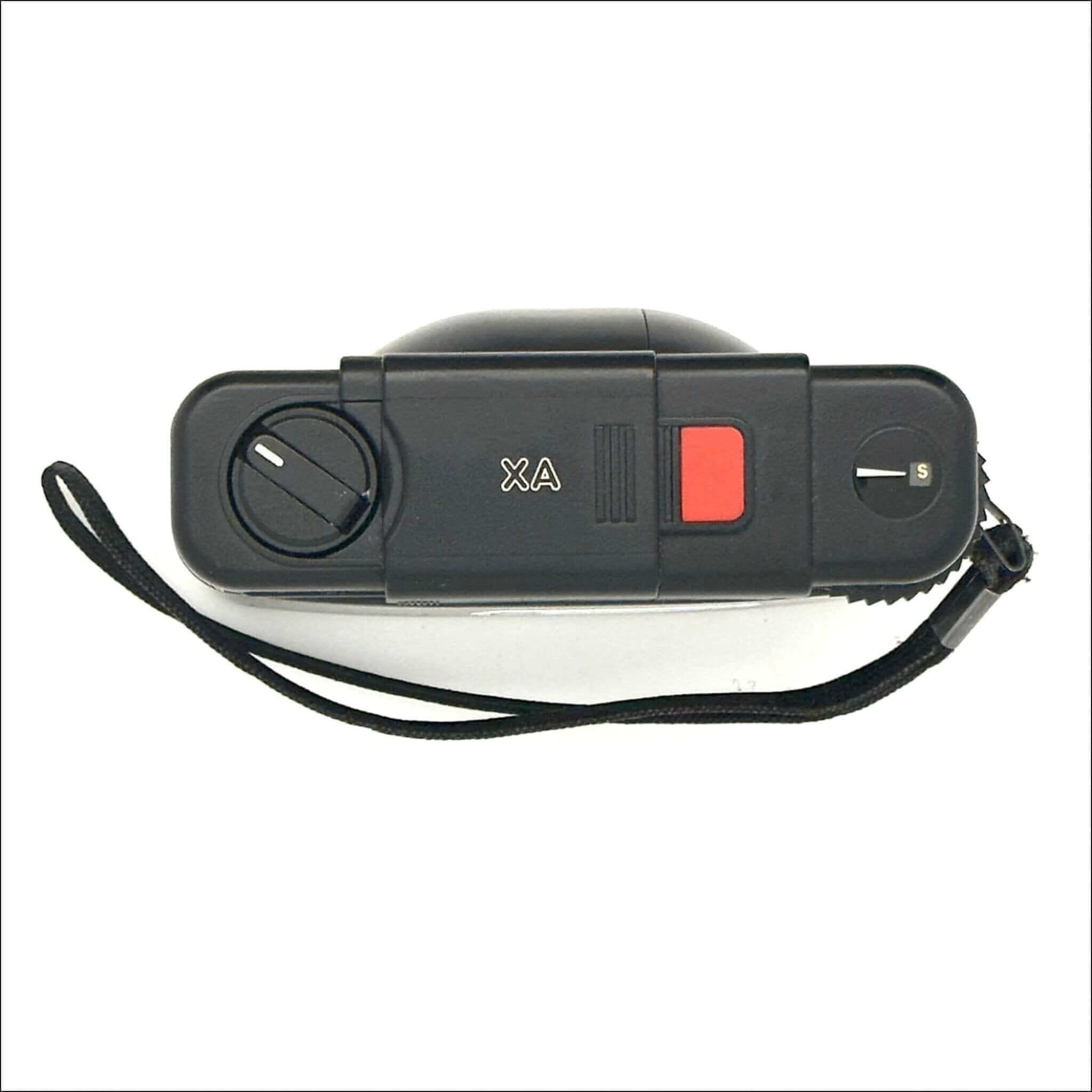 Black compact camera with red shutter button and ’xa’ branding on the top panel.