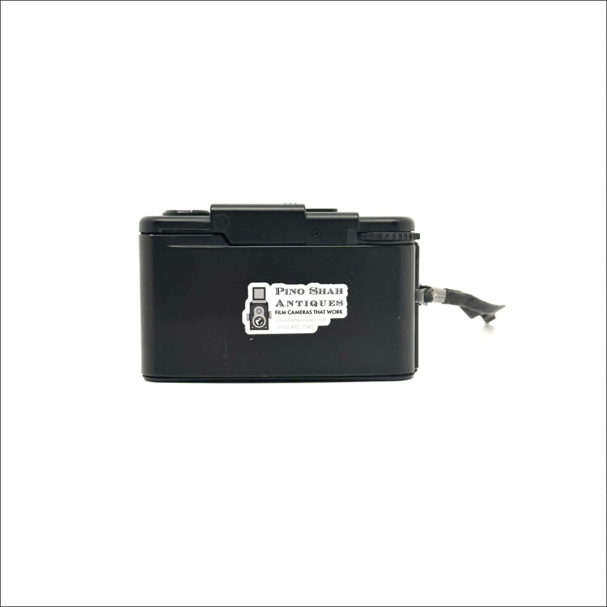 Black plastic box camera with a white sticker reading ’pino shar antiques film cameras that work’ on its side.