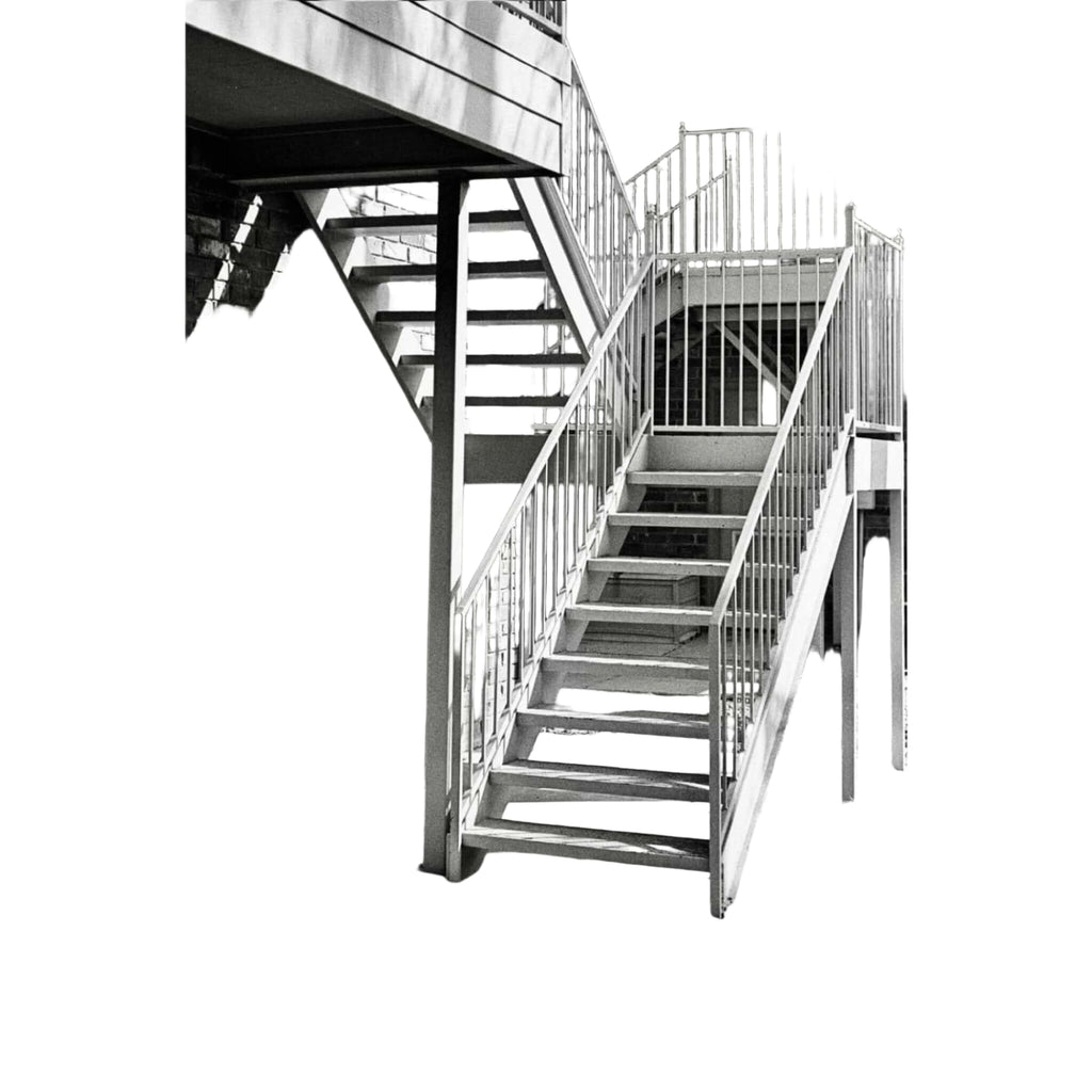 Metallic staircase with vertical railings and concrete steps against a brick wall