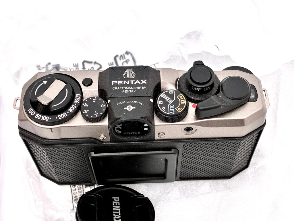 Silver and black pentax k-100 35mm half-frame film camera with textured grip dials and craftsmanship label on top plate