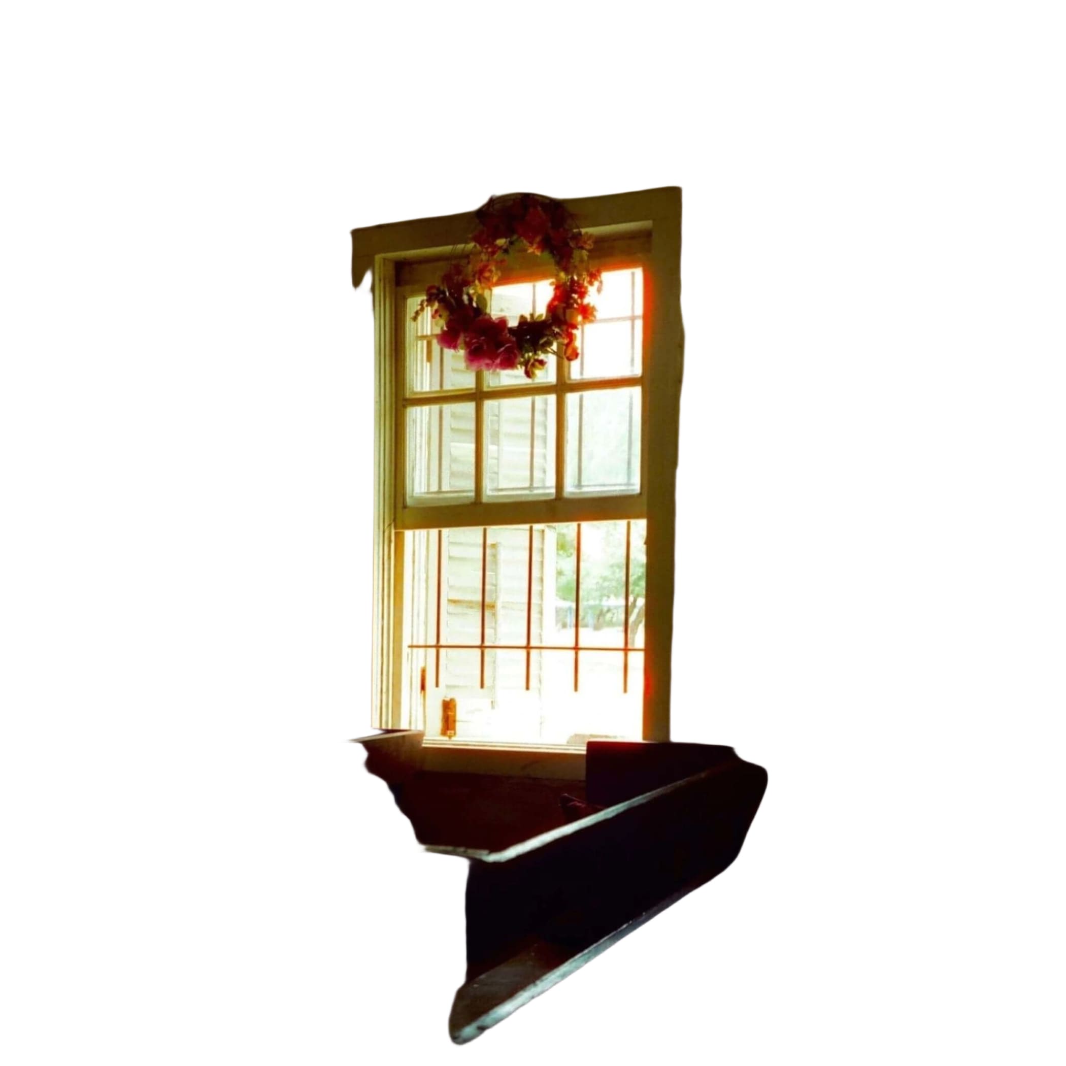 A floral wreath with red and pink blossoms hangs above a window in an old, sunlit room.