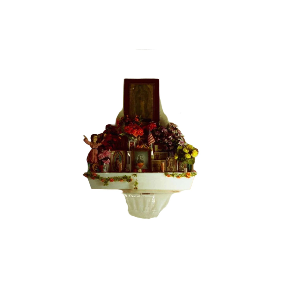 A white altar adorned with vibrant red, pink, and yellow flowers arranged in lush bouquets on either side of a central religious statue.