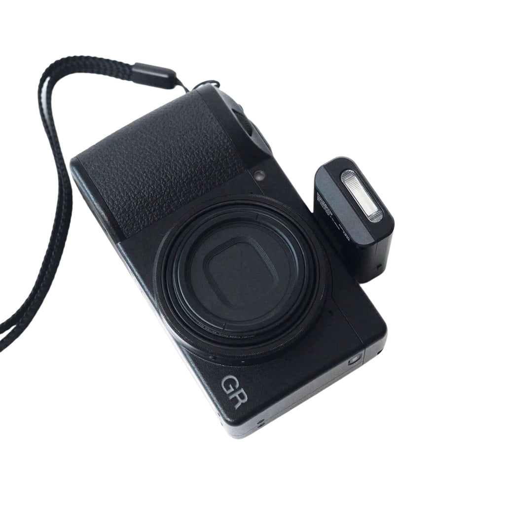 Black gr series compact camera with textured grip and attached flash unit.