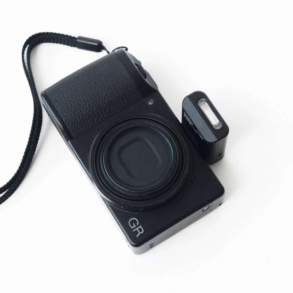 Black gr series compact camera with textured grip and attached flash unit.