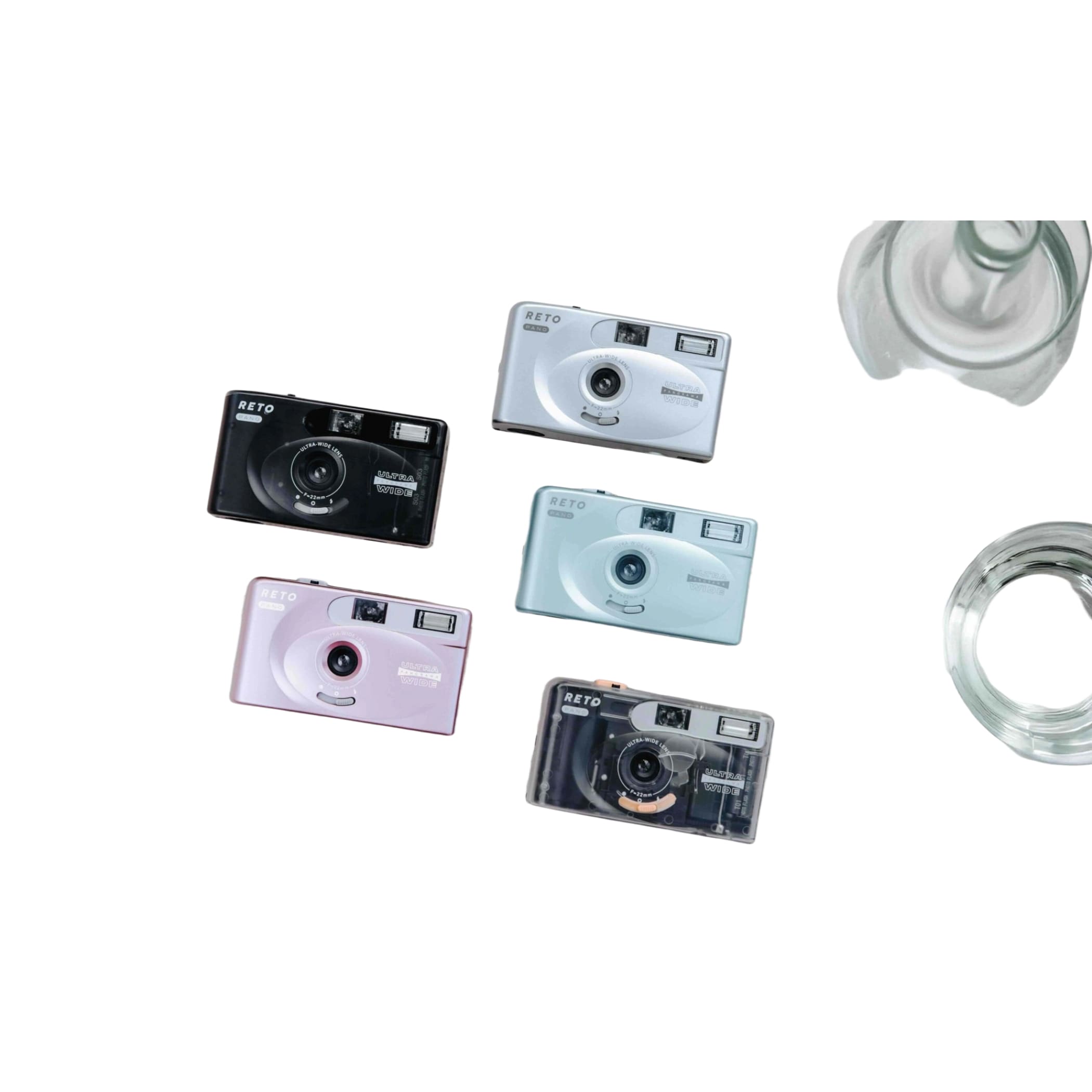 Five compact reto brand instant cameras in black, silver, light blue, pink and transparent with orange accents.